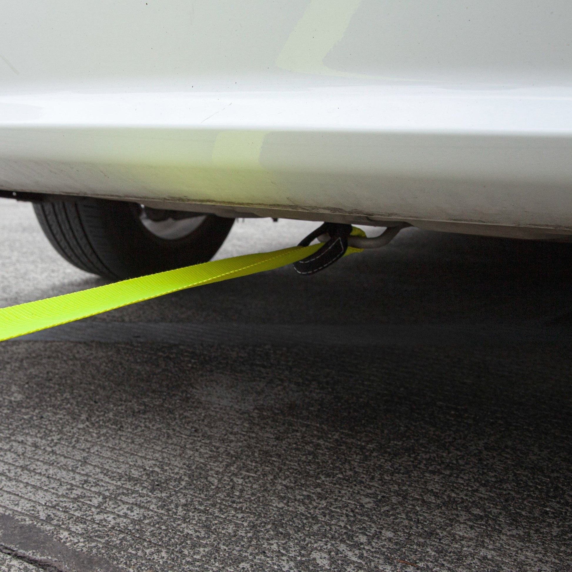 Close-up of a car's undercarriage with a yellow strap attached, on a carpeted floor.